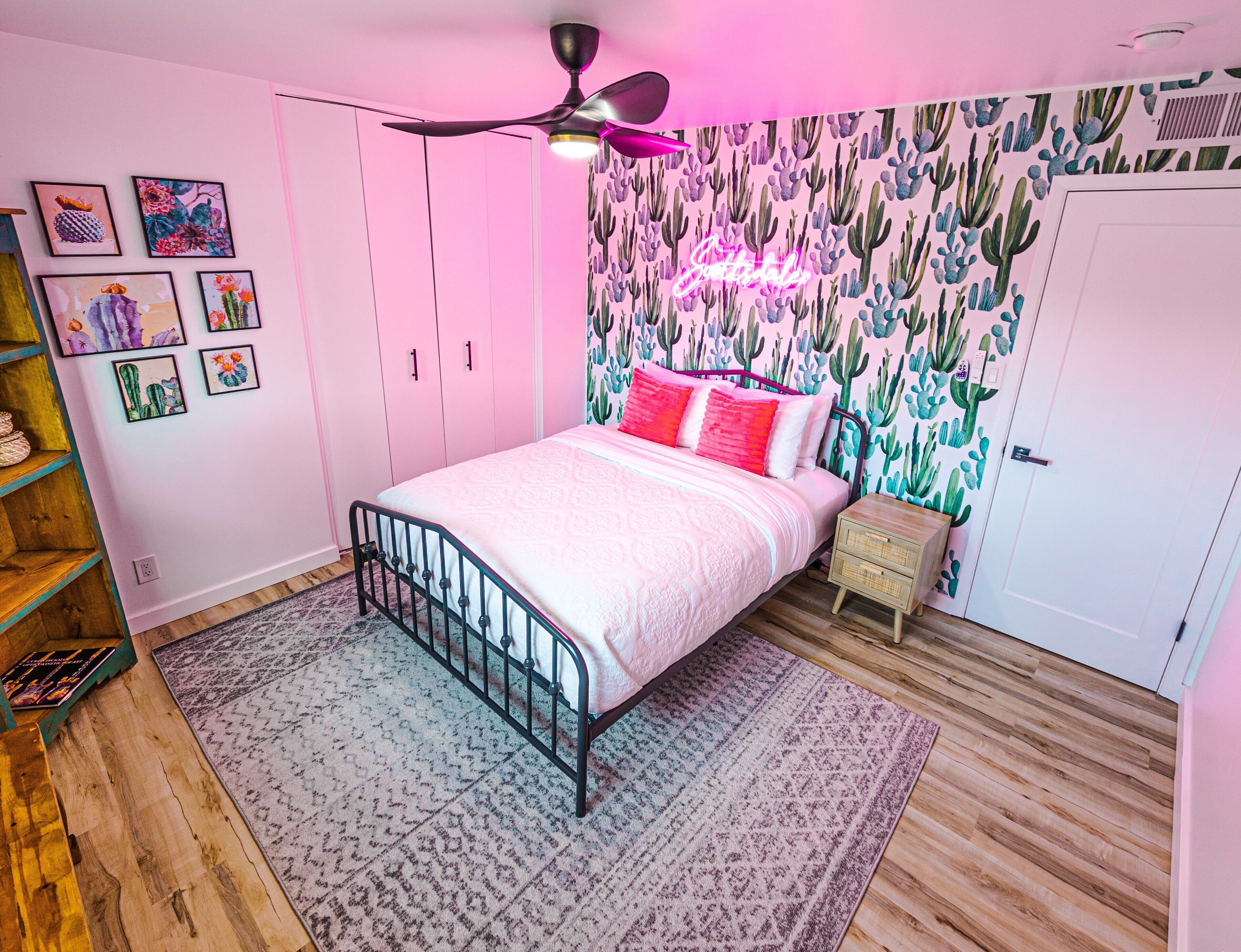 A bedroom with a bed, a ceiling fan, a cactus-themed wallpaper, and a bookshelf.