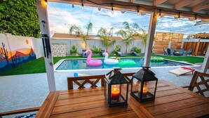 A wooden table with a lantern and a candle, overlooking a swimming pool with inflatable flamingos and a mural on the wall. - Four Palms - Pool BBQ Fire Pit - 5 min to Old Town (Scottsdale)