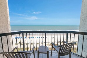 A balcony with a view of the beach, featuring chairs and a table.