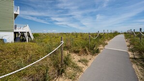 Um caminho leva a um edifício com varanda, cercado por vegetação e céu claro.