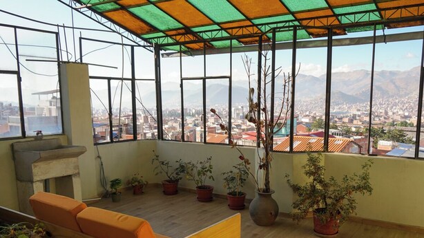 Ein geräumiger Balkon mit Holzbank und Topfpflanzen, mit Blick auf eine Stadtlandschaft und entfernte Berge.
