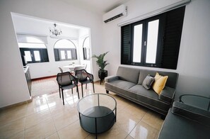 A modern living room with a sofa, a glass coffee table, and a dining area with chairs and a table.