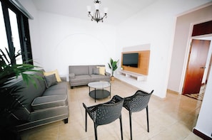 Una sala moderna con sofá, mesa de centro y dos sillones, un televisor de pantalla plana montado en la pared y un ventanal grande.