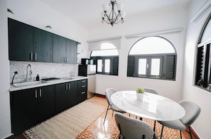 A modern kitchen with dark cabinets, a marble countertop, and a dining area with a round table and chairs. - Historic Colonial Apt: Fast Wi-Fi, Free Parking (San Juan)