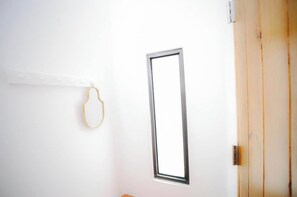 Un mur blanc avec une fenêtre rectangulaire et une porte dotée d’un cadre en bois.