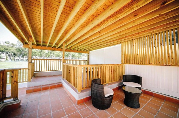 Un espace extérieur abrité, doté de poutres en bois, d’un mur blanc et de deux fauteuils en osier avec des coussins.