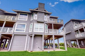 A multi-story building with balconies, a covered porch, and a grassy yard.