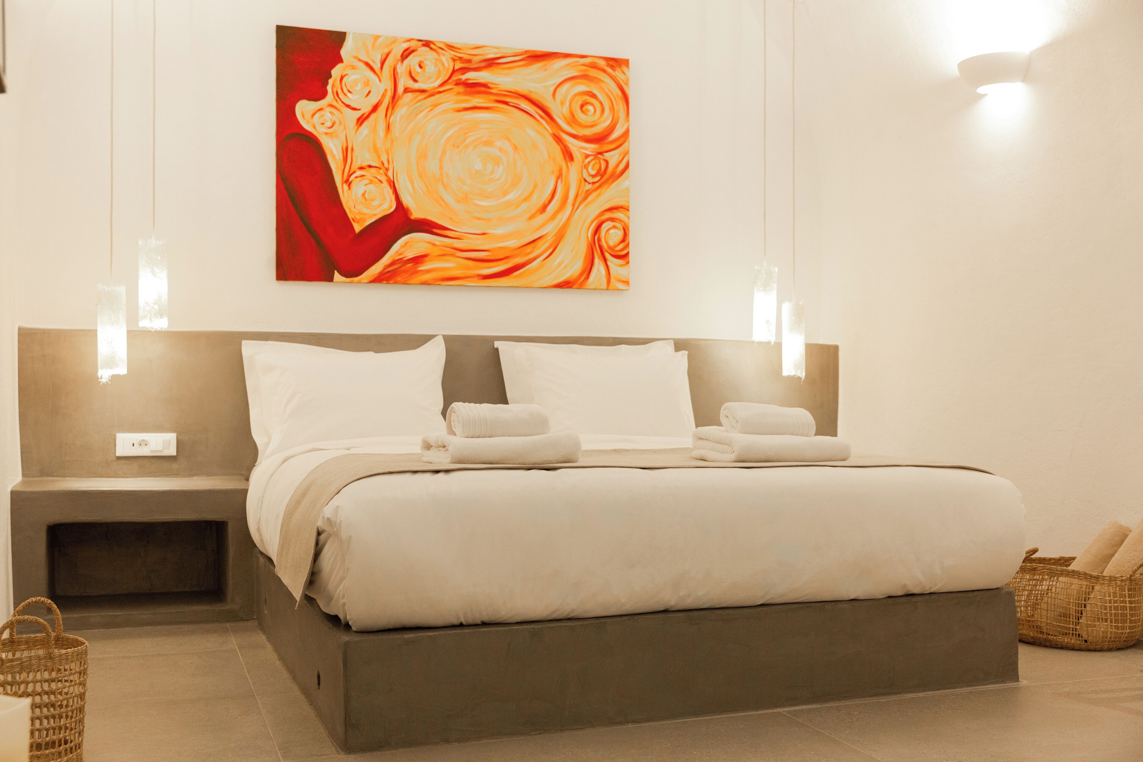 A modern hotel room with a large bed, bedside tables, a wall-mounted painting, and a basket on the floor.
