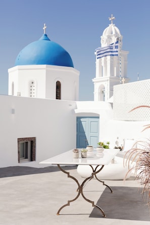 A white building with a blue dome and a clock tower, a white table with metal legs, and potted plants.