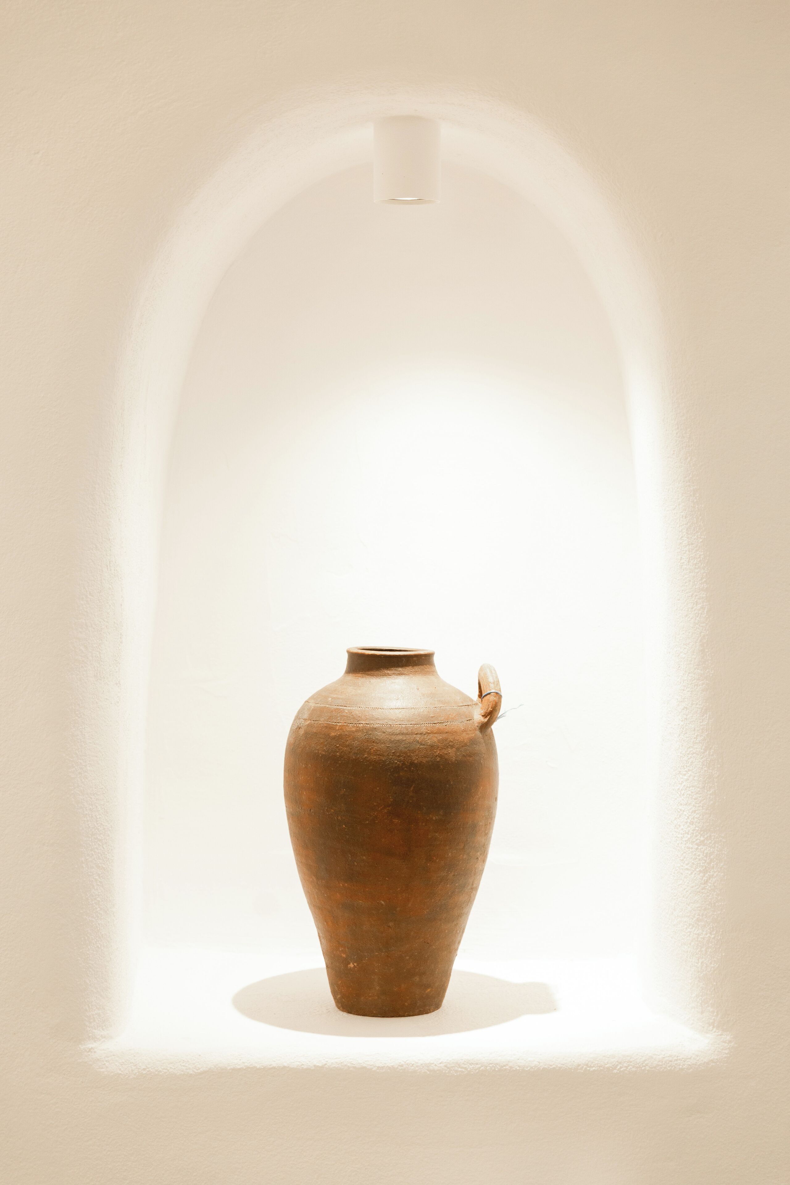 A single pottery vase in a white-walled alcove with a spotlight.