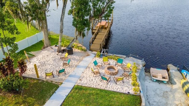 A lakeside outdoor seating area with a fire pit, lounge chairs, and a dock extending into the water. - * Beautiful Lakehouse with Pool and Movie Theater* (Casselberry)