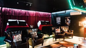 A room with two beds, leather armchairs, a small table, and a neon light. - * Beautiful Lakehouse with Pool and Movie Theater* (Casselberry)
