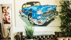 A living room with a brown leather sofa, a round wooden coffee table with a white vase, and a large painting of a blue car on the wall. - * Beautiful Lakehouse with Pool and Movie Theater* (Casselberry)