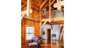 A spacious room with wooden beams, a balcony, a staircase, and a leather armchair.