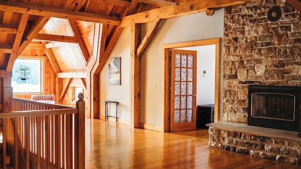 A spacious loft with high ceilings, wooden beams, a stone fireplace, and a view of the outdoors.