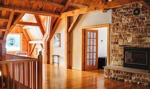 Une pièce spacieuse avec une cheminée en pierre, des poutres apparentes et une vue sur l’extérieur.