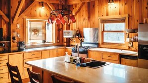A wooden cabin kitchen with a central island, wooden cabinets, and a hanging pot rack.