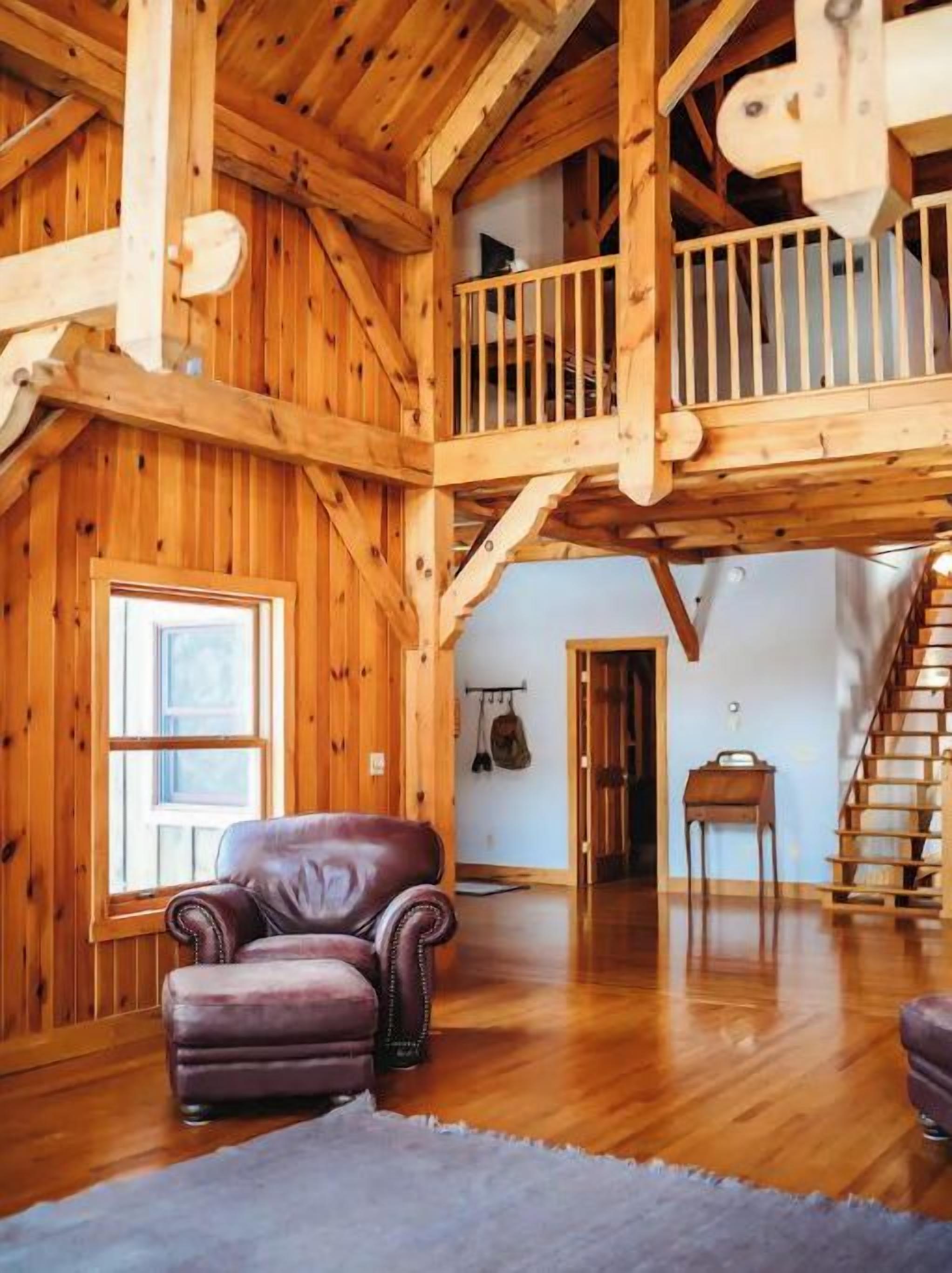 A spacious room with wooden beams, a balcony, a staircase, and a leather armchair.