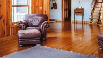 A spacious room with wooden beams, a balcony, a staircase, and a leather armchair.