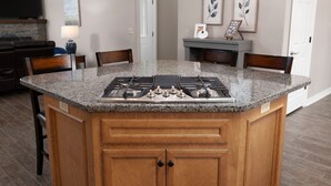 Una isla de cocina con encimera de granito, estufa a gas y armarios de madera.