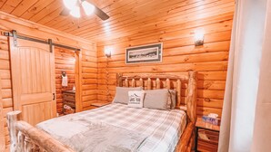 Ein Schlafzimmer einer Holzhütte mit einem Bett, einem Nachttisch, einer Kommode und einem Deckenventilator.