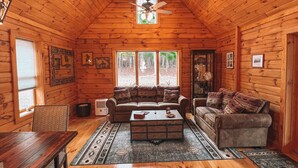 Ein gemütliches Blockhaus mit Holzwänden, einem Deckenventilator, einer Couch, einem Couchtisch und einem Esstisch.