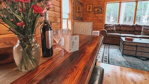 Ein Holzinterieur mit Essbereich, inklusive Holztisch, Blumenvase, Weinflasche und einer Couch.