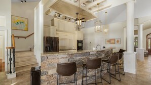 A spacious kitchen with a stone island, bar stools, and modern lighting fixtures.