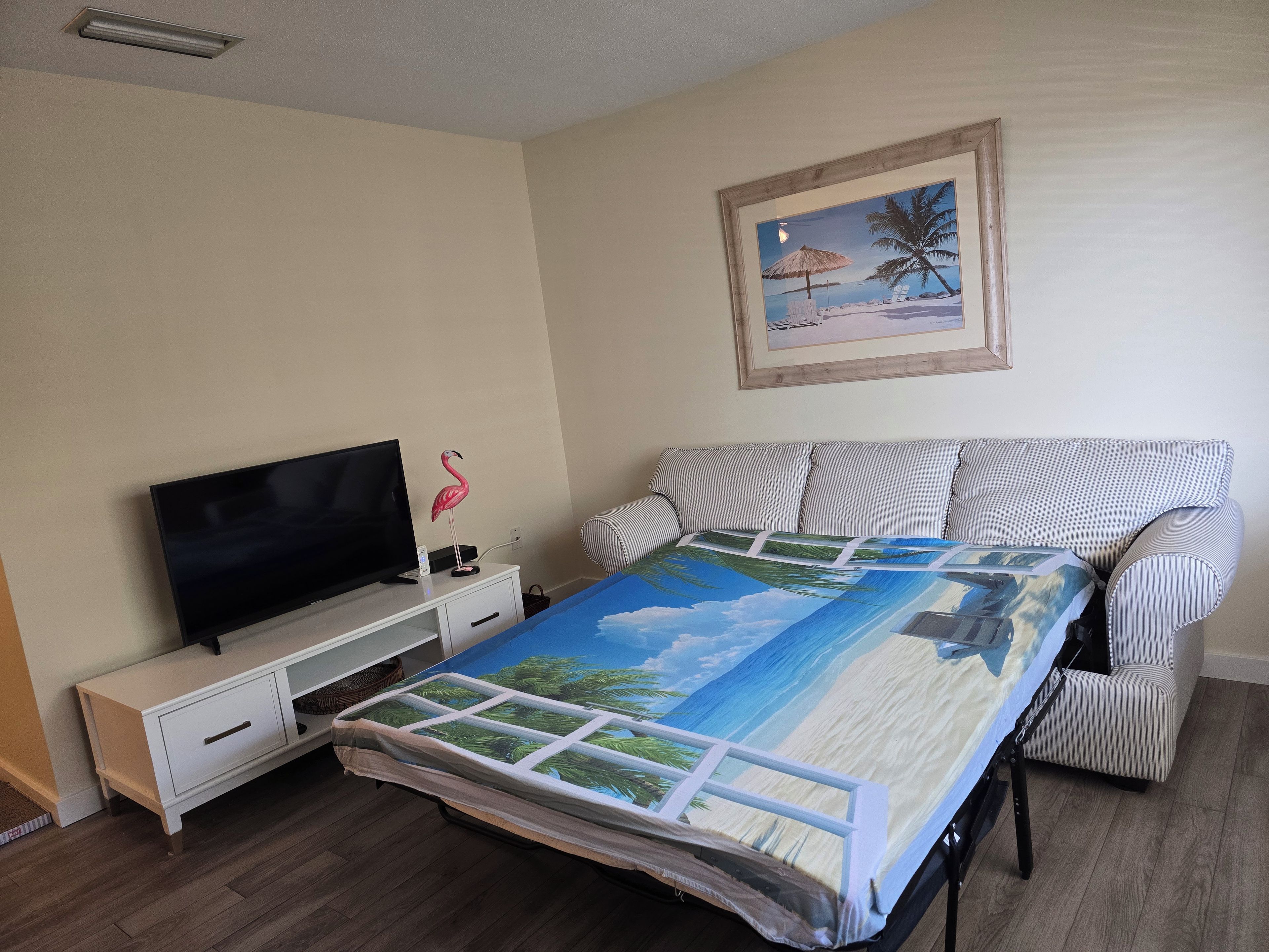 A bedroom with a bed, a television, a nightstand, a framed picture, and a striped sofa.