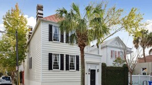 A two-story white building with black shutters, a red roof, and a palm tree in front. - Private Pool & Historic Home-‘The Walled Garden’ (Charleston)