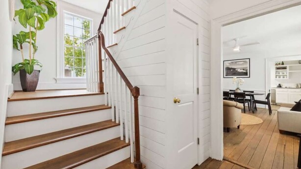 A staircase with wooden steps and white walls, leading to a room with a dining area and a view of the outdoors. - Private Pool & Historic Home-‘The Walled Garden’ (Charleston)