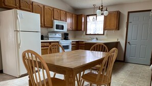 A kitchen with wooden cabinets, a white refrigerator, a microwave, a stove, and a dining table with four wooden chairs. - The Pines of Apple Valley, 31 Beautiful Vacation Condos. (Howard)