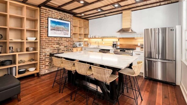 A modern kitchen with a large island, wooden shelves, and a stainless steel refrigerator. - Historic Boutique Home ‘Tuckertown’ (Charleston)