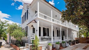 A white two-story house with a front porch, a 'ONE WAY' sign, and a brick pathway leading to the entrance. - Historic Boutique Home ‘Tuckertown’ (Charleston)