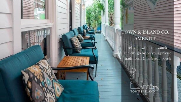 Eine traditionelle Veranda in Charleston mit türkisblauen Sofas und Holztischen, die einen Blick ins grüne Umland bietet.