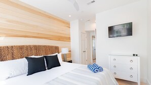 Una habitación de hotel moderna con cabecera de madera, una cama grande con ropa de cama blanca, un aparador blanco y un televisor de pantalla plana en la pared.