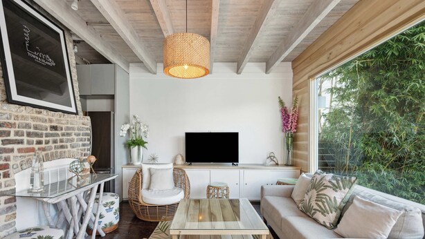 A cozy living room with a TV, wicker furniture, and a large window overlooking greenery. - Private Pool & Historic Home - ‘Sugarsweet House’ (Charleston)