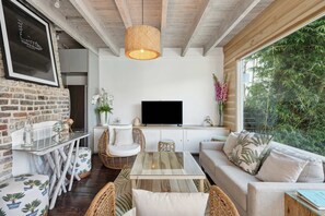 Una sala de estar acogedora con televisor, muebles de mimbre y un amplio ventanal con vistas a la vegetación.