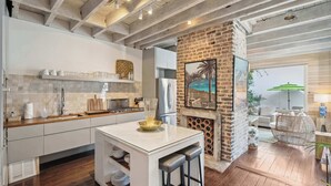A modern kitchen with a central island, white cabinetry, and a brick accent wall. - Private Pool & Historic Home - ‘Sugarsweet House’ (Charleston)