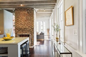A kitchen with a brick wall, a dining area with a glass table, and a living room with a sofa. - Private Pool & Historic Home - ‘Sugarsweet House’ (Charleston)