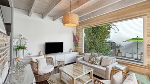 A modern living room with a TV, wicker furniture, and a large window with a view of greenery. - Private Pool & Historic Home - ‘Sugarsweet House’ (Charleston)