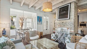 A spacious living area with a glass coffee table, wicker furniture, and a brick accent wall. - Private Pool & Historic Home - ‘Sugarsweet House’ (Charleston)