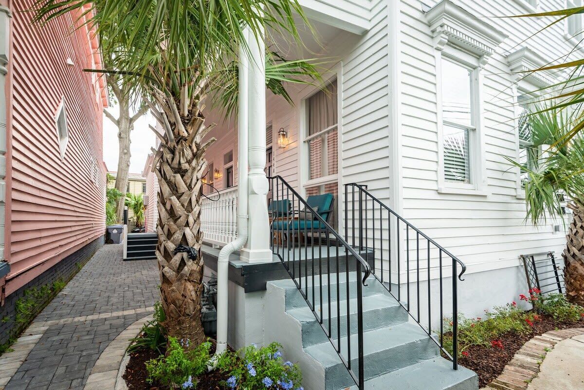 A white house with a porch, a palm tree, and a brick pathway.