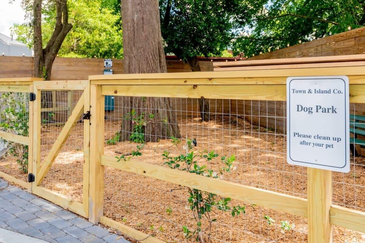 Een houten poort naar een hondenpark met een bord waarop staat: Town & Island Co. Hondenpark. Gelieve na uw huisdier op te ruimen.