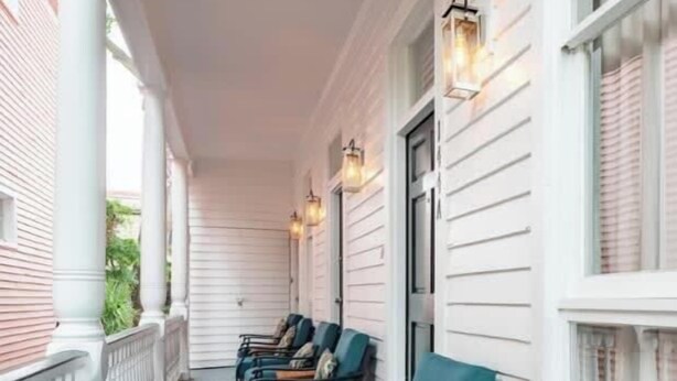 A covered porch with white railings, teal chairs, and wooden tables. - Boutique Historic Home ‘The Cisco’ (Charleston)