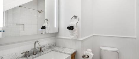 A modern bathroom with a marble sink, a large mirror, a toilet, and a towel rack.