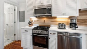 A compact kitchen with white cabinetry, a stainless steel microwave, a gas stove, a toaster, and a coffee maker. - Boutique Historic Home ‘The Cisco’ (Charleston)