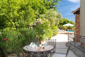 Eine Terrasse mit einem runden Esstisch, umgeben von üppigem Grün und einem Pool im Hintergrund.