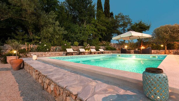 A swimming pool with lounge chairs and an umbrella, surrounded by stone walls and trees. - Villa LEMON BELLISSIMA (Ljutići)