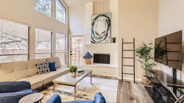 A spacious living room with a sofa, coffee table, and blue armchairs. A fireplace and abstract art are on the wall. - Townhome Medical Ctr/Six Flags/La Cantera/Rim (San Antonio)